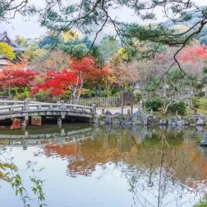 Parco Maruyama Kyoto in autunno con ponte in pietra e foglie rosse di acero giapponese.