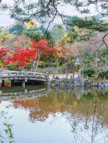 Parco Maruyama Kyoto in autunno con ponte in pietra e foglie rosse di acero giapponese.